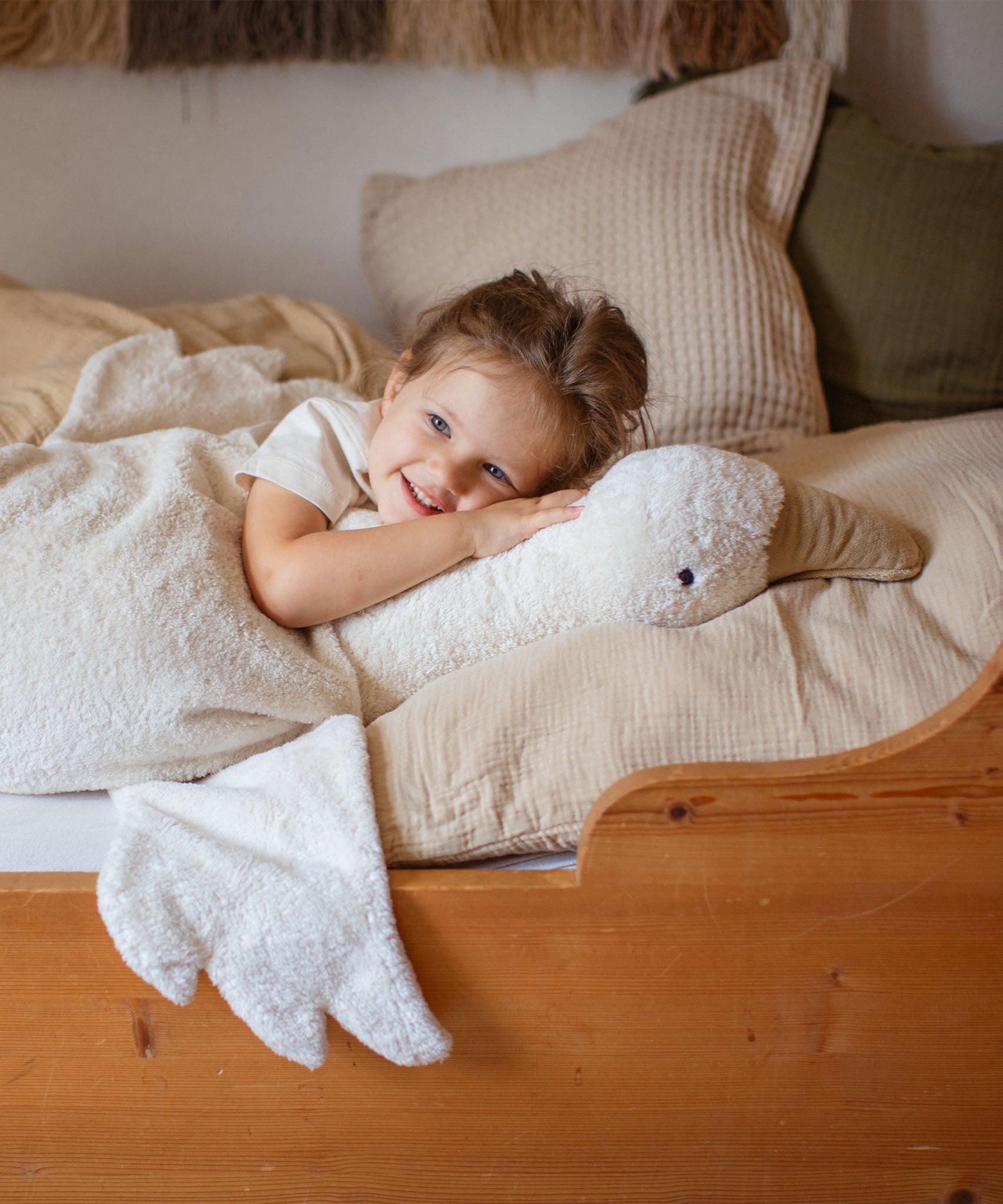 A close up of a small child lying next to the white Senger XL goose. A organic heatable soft toy made from GOTS cotton plush and natural wool.