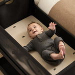 A small baby laying in the SnuzPod5 black wooden bedside cot, in a grey babygrow.