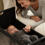 A woman watching over her baby from bed, with the SnuzPod5 close to her bedside.