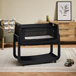 The black graphite wooden SnuzPod5 bedside crib with wheels, that has been wheeled into the living room 