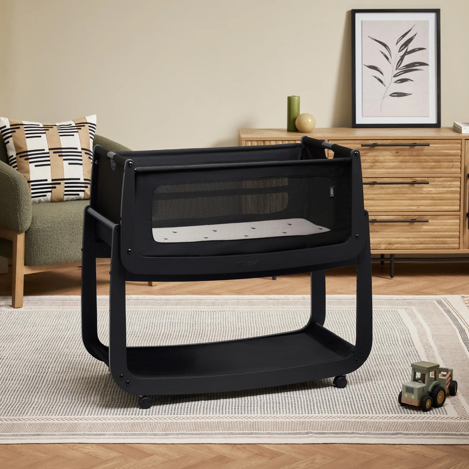 The black graphite wooden SnuzPod5 bedside crib with wheels, that has been wheeled into the living room 