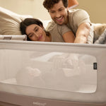 Two parents lovingly loom at their baby in a SnuzPod5, from the comfort of their own bed.