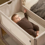 A small baby laying in the SnuzPod5 natural wooden bedside cot, in a brown babygrow.