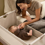 A woman smiling at her baby from bed, with the SnuzPod5 close to her bedside.