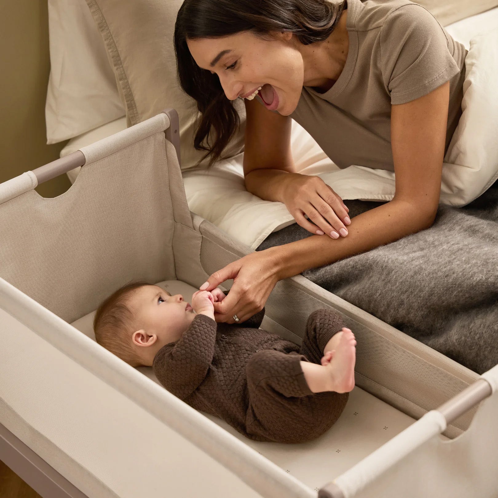 A woman smiling at her baby from bed, with the SnuzPod5 close to her bedside.