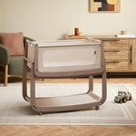 The mocha coloured wooden SnuzPod5 bedside crib with wheels, that has been wheeled into the living room