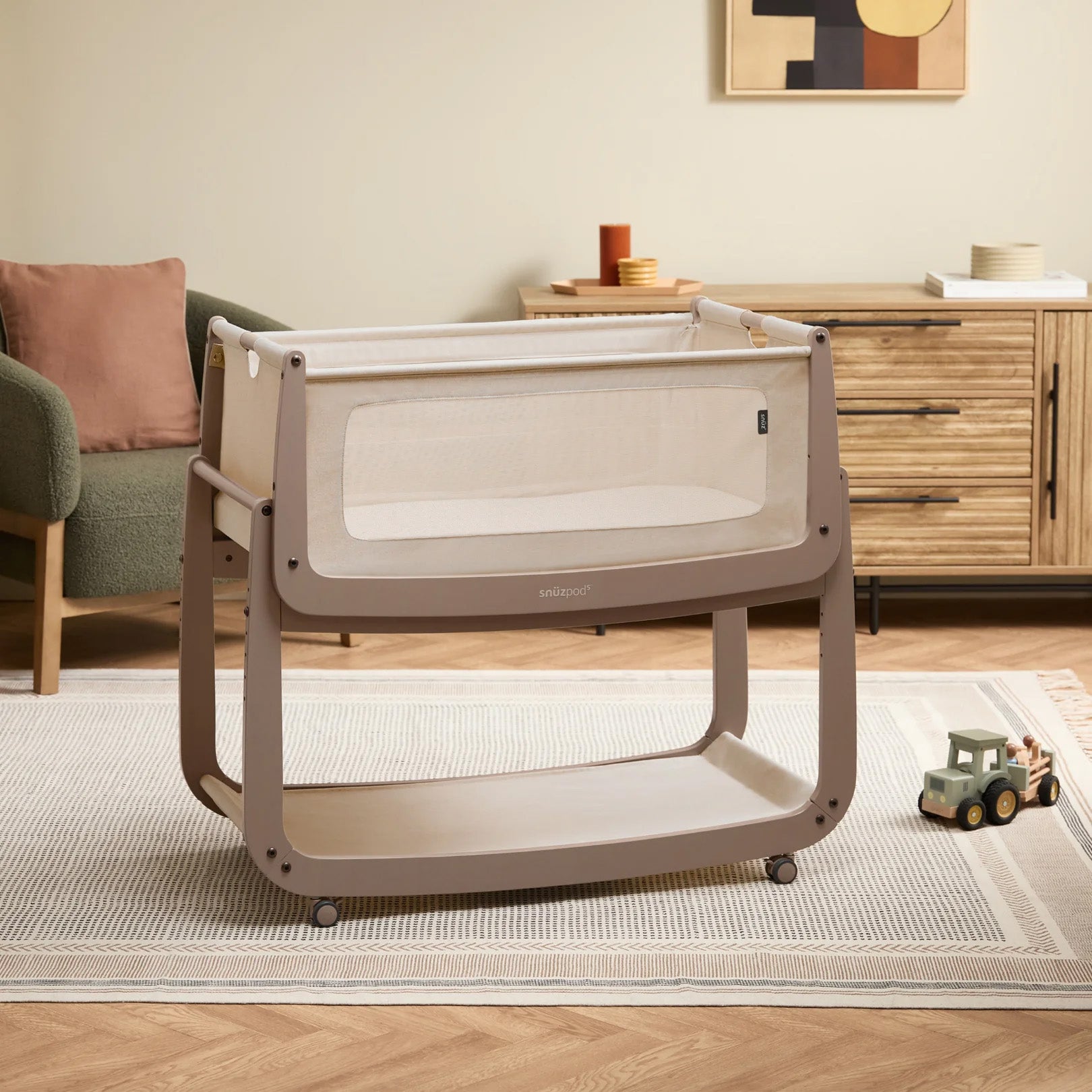 The mocha coloured wooden SnuzPod5 bedside crib with wheels, that has been wheeled into the living room