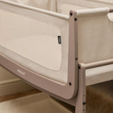 A closeup of the corner of the mocha coloured wooden SnuzPod5 bedside crib, showing where the bassinet can detach from the main rocking frame. 