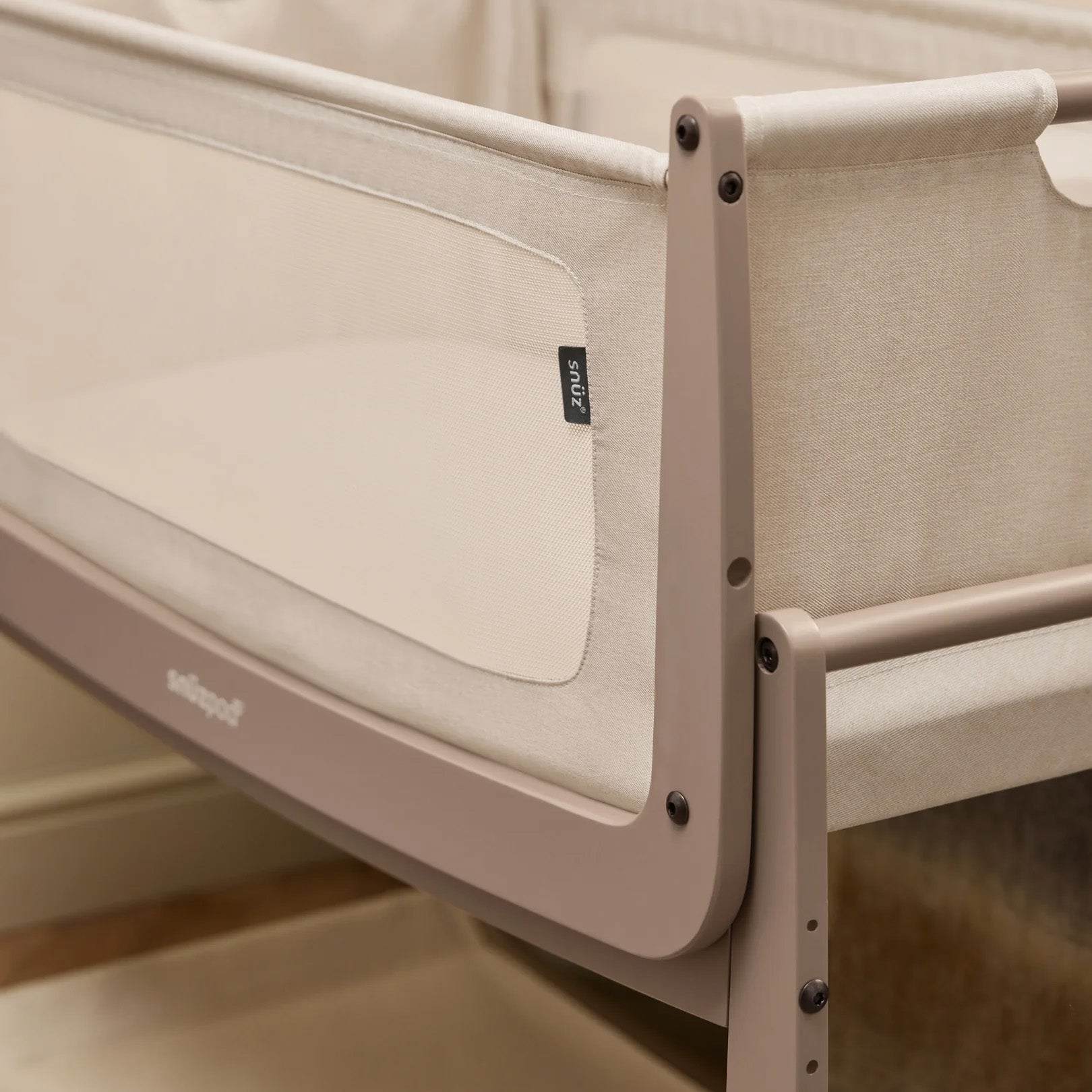 A closeup of the corner of the mocha coloured wooden SnuzPod5 bedside crib, showing where the bassinet can detach from the main rocking frame. 