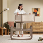 A woman detaching the SnuzPod5 bassinet from the main rocking frame, showing how easily portable this baby cot is.