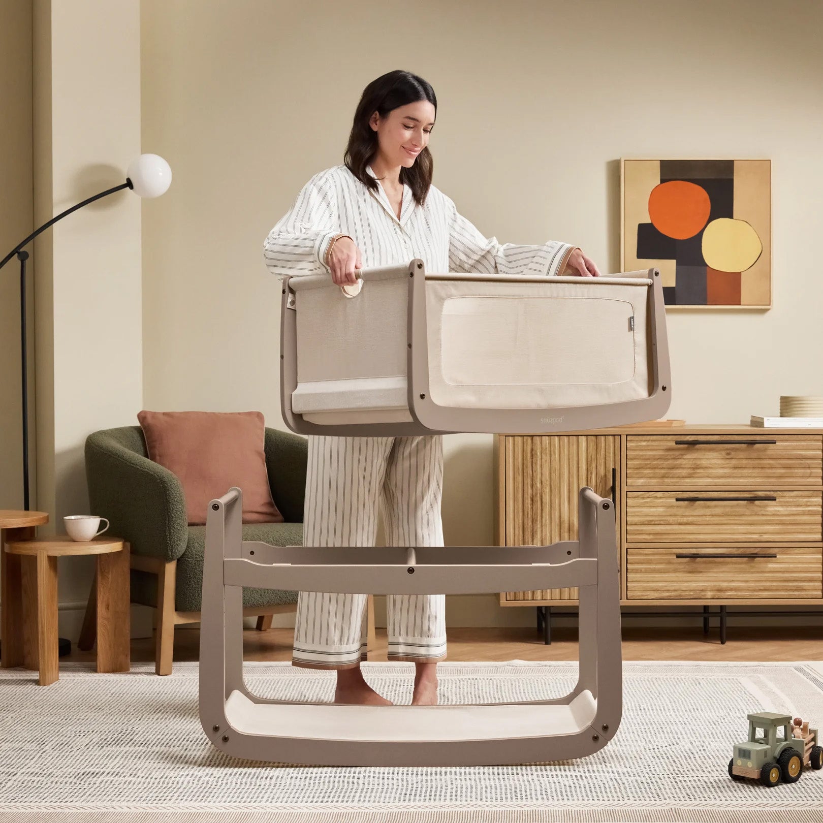 A woman detaching the SnuzPod5 bassinet from the main rocking frame, showing how easily portable this baby cot is.