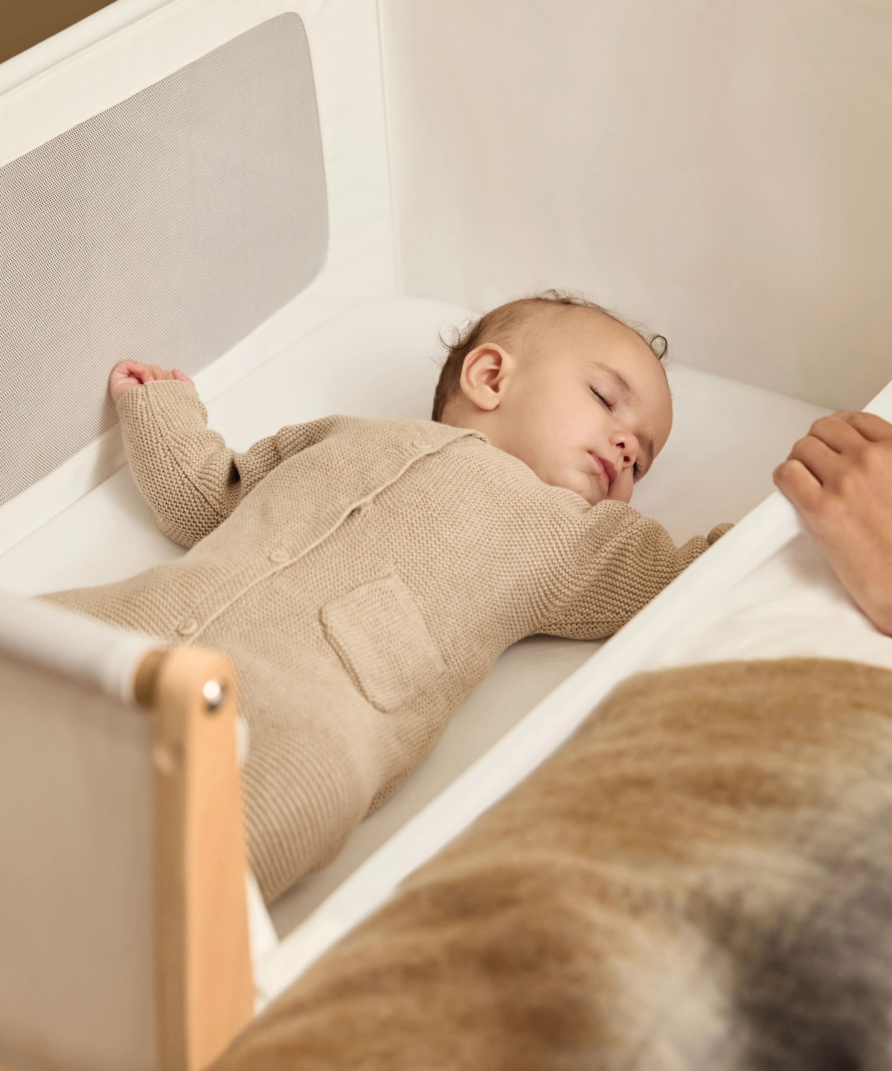 A small baby sleeping in the SnuzPod5 natural wooden bedside cot, in a cream babygrow.