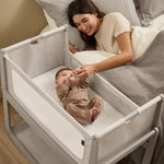 A woman watching over her baby from bed, with the SnuzPod5 close to her bedside.