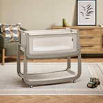 The light grey wooden SnuzPod5 bedside crib with wheels, that has been wheeled into the living room 