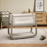 The light grey wooden SnuzPod5 bedside crib with wheels, that has been wheeled into the living room 