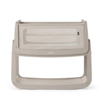 The SnuzPod5 bedside baby crib with a light grey wooden frame, light grey mesh sides, and a white mattress. 