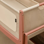 A closeup of the corner of the Terracotta wooden SnuzPod5 bedside crib, showing where the bassinet can detach from the main rocking frame. 