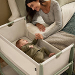 A woman watching over her baby from bed, with the SnuzPod5 close to her bedside.
