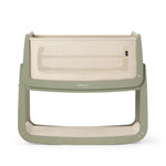 The SnuzPod5 bedside baby crib with a sage green wooden frame, cream mesh sides, and a white mattress. 