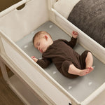 A small baby sleeping in the SnuzPod5 white wooden bedside cot, in a brown babygrow.