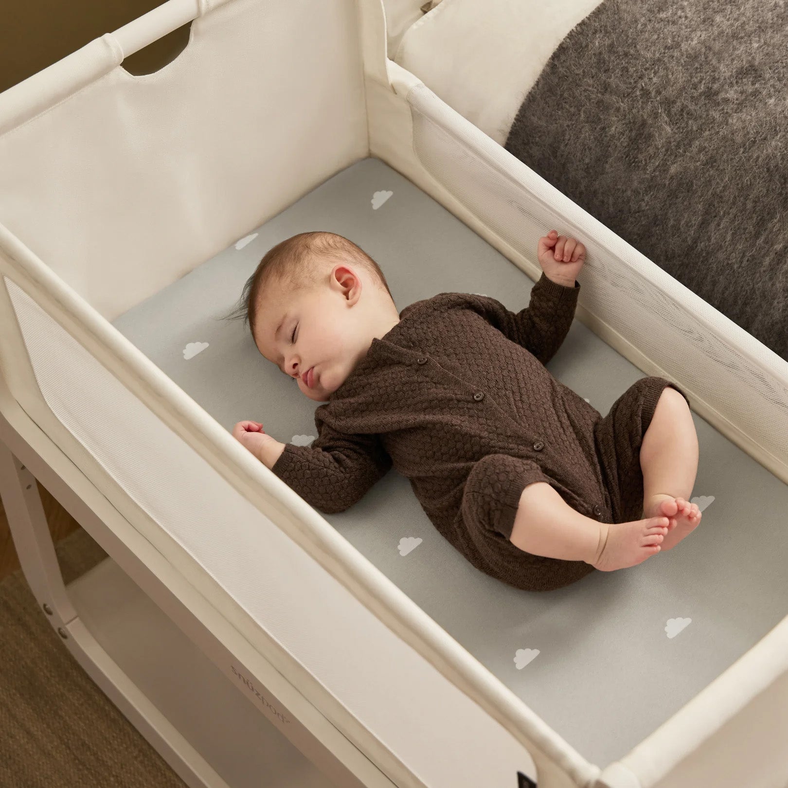 A small baby sleeping in the SnuzPod5 white wooden bedside cot, in a brown babygrow.