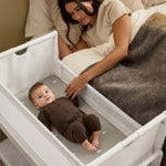 A woman watching over her baby from bed, with the SnuzPod5 close to her bedside.
