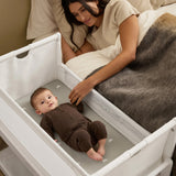 A woman watching over her baby from bed, with the SnuzPod5 close to her bedside.