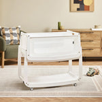 The natural wooden SnuzPod5 bedside crib with wheels, that has been wheeled into the living room.