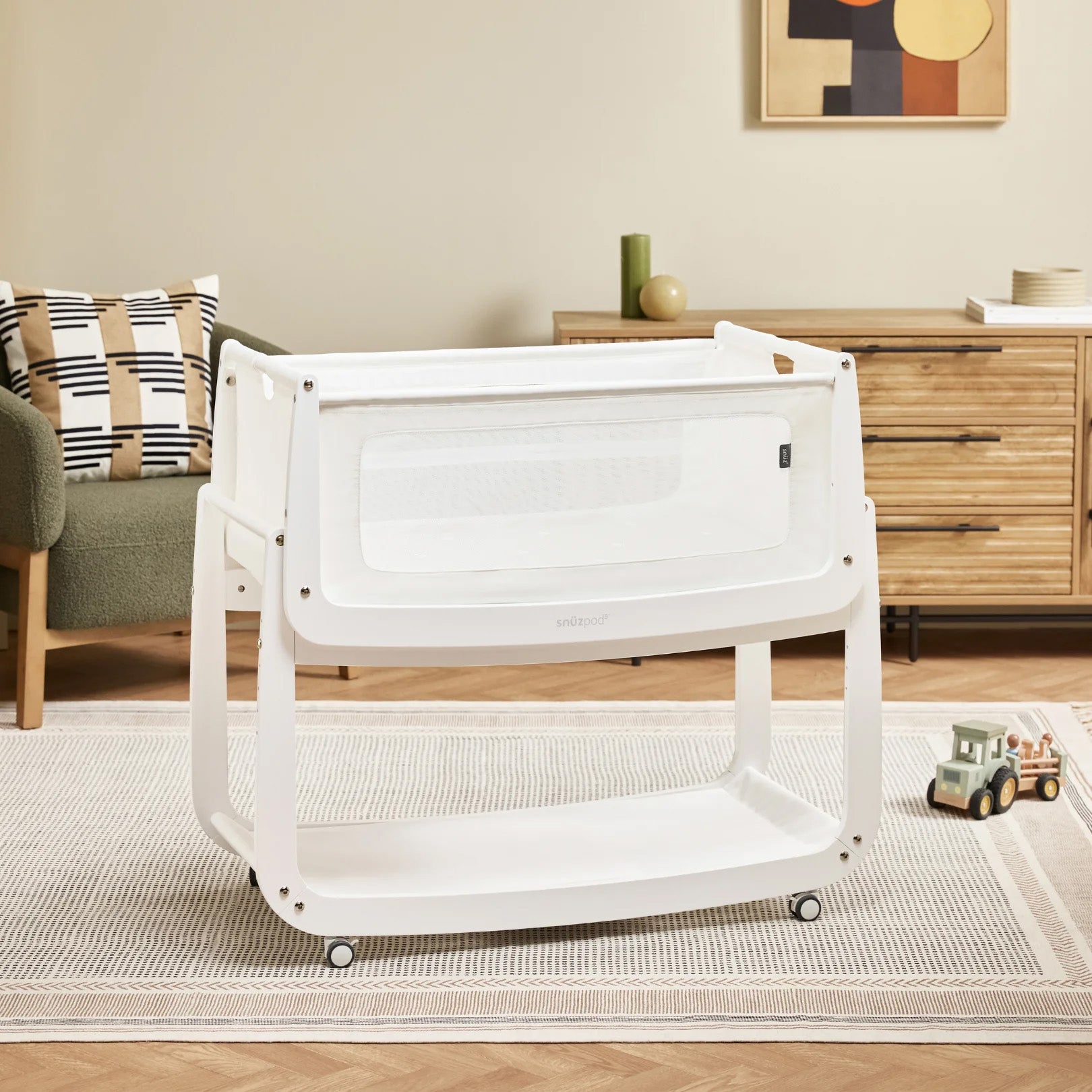 The natural wooden SnuzPod5 bedside crib with wheels, that has been wheeled into the living room.