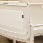 A closeup of the corner of the white wooden SnuzPod5 bedside crib, showing where the bassinet can detach from the main rocking frame. 