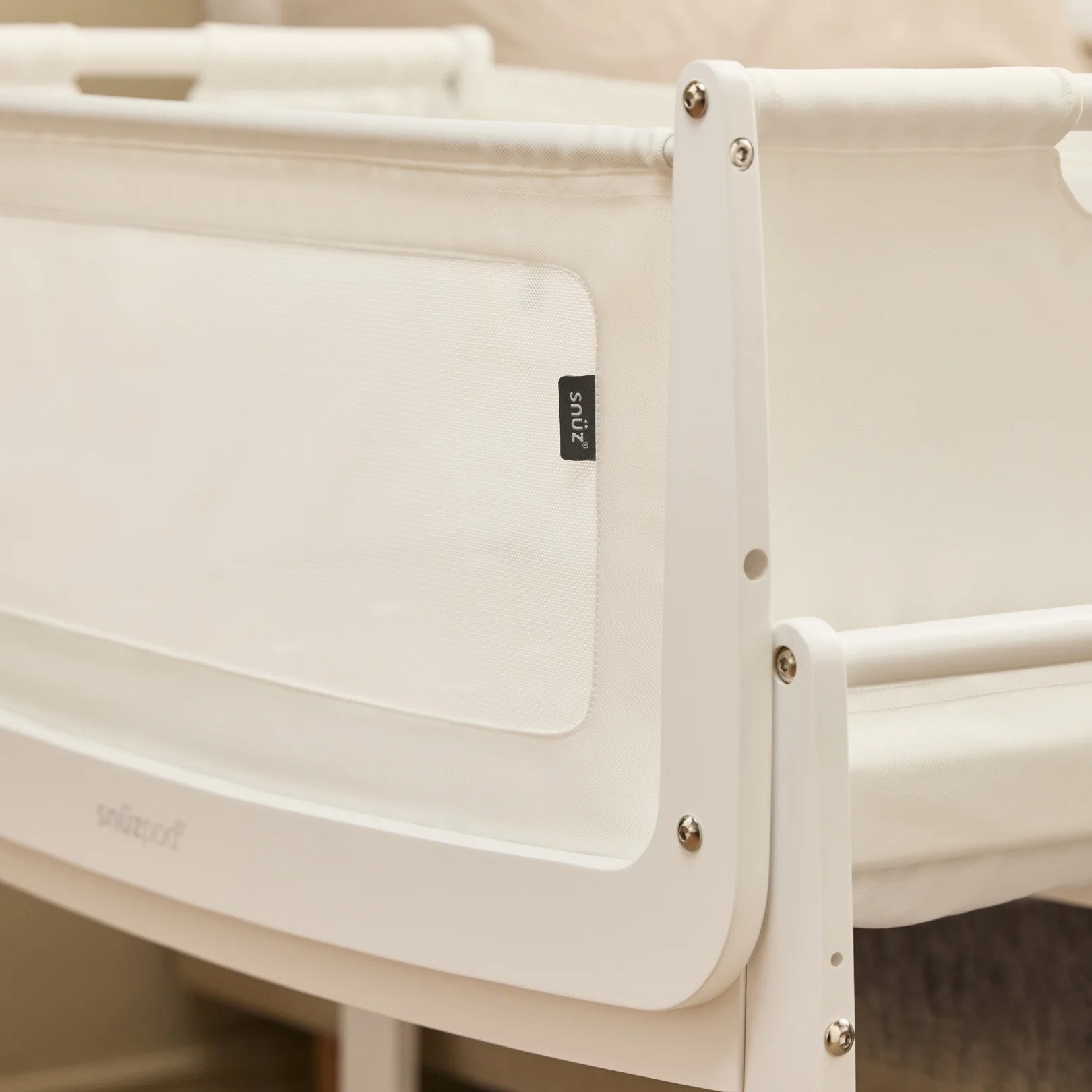 A closeup of the corner of the white wooden SnuzPod5 bedside crib, showing where the bassinet can detach from the main rocking frame. 