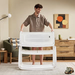 A man detaching the SnuzPod5 bassinet from the main rocking frame, showing how easily portable this baby cot is.

