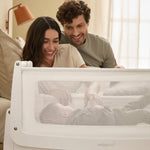 Two parents watching their baby in a SnuzPod5 bedside cot, from the comfort of their own bed.