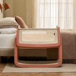 The SnuzPod 5 bedside baby crib with a lovely terracotta pink wooden frame, next to an adult's bed in a beautifully decorated bedroom.
