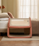 The SnuzPod 5 bedside baby crib with a lovely terracotta pink wooden frame, next to an adult's bed in a beautifully decorated bedroom.