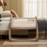 The SnuzPod 5 bedside baby crib with a lovely pale brown wooden frame, next to an adult's bed in a beautifully decorated bedroom.