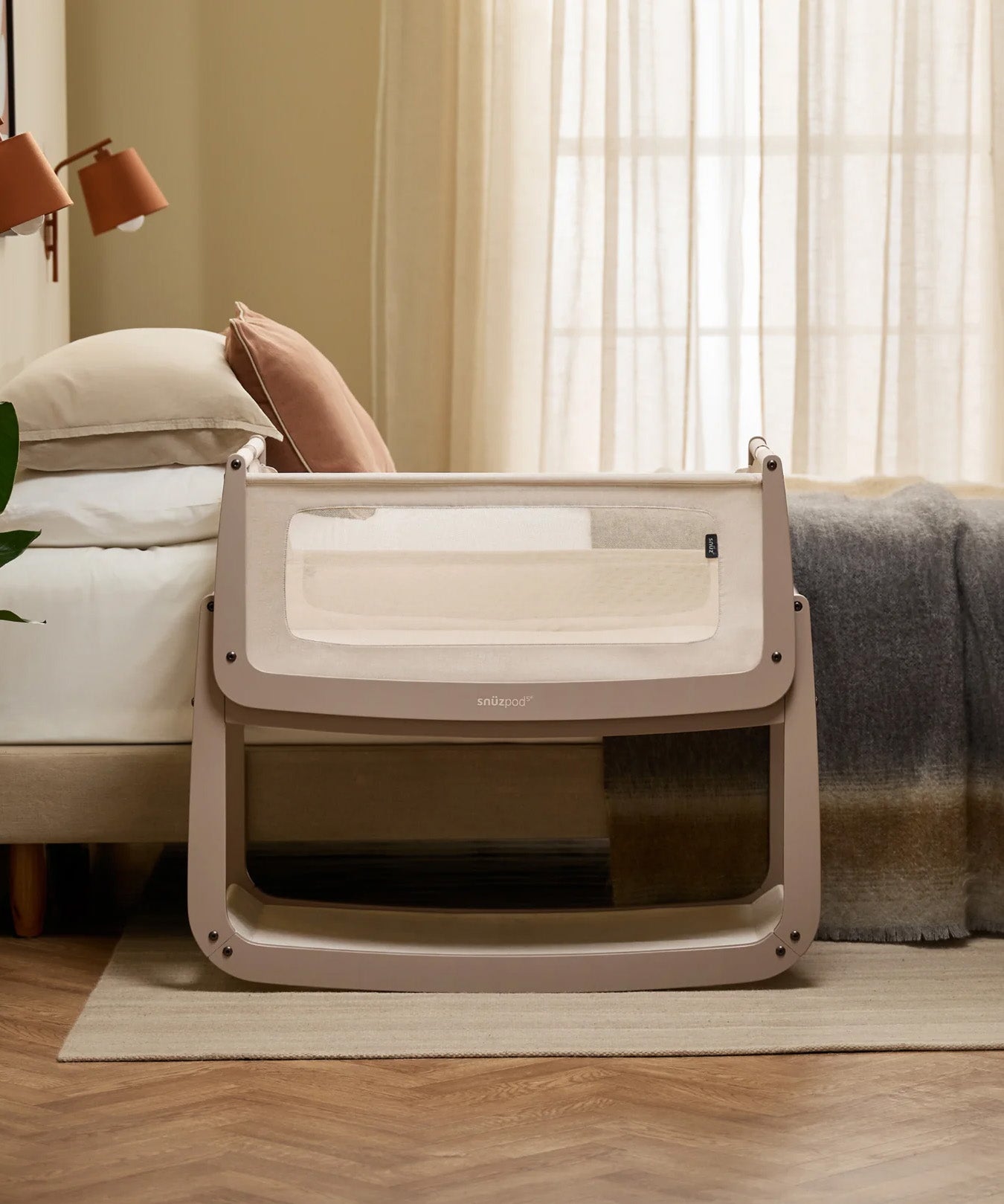 The SnuzPod 5 bedside baby crib with a lovely pale brown wooden frame, next to an adult's bed in a beautifully decorated bedroom.