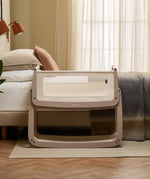 The SnuzPod 5 bedside baby crib with a lovely pale brown wooden frame, next to an adult's bed in a beautifully decorated bedroom.