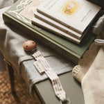 Avery Row Pacifier Holder in Stripe, next to a small pile of Beatrix Potter books and baby blankets