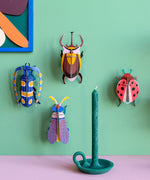 Wall display showing different Studio Roof 3D beetle cardboard wall art sets with a candle in front