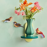 3 Studio Roof birds on a light green wall, with a vase full of colourful flowers on a small shelf also on a wall. The birds are the Sparrows and the Cardinal