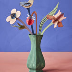 The Studio Roof Cardboard Bouquet - William Morris inside a green painted vase, on a blue/purple and peach background