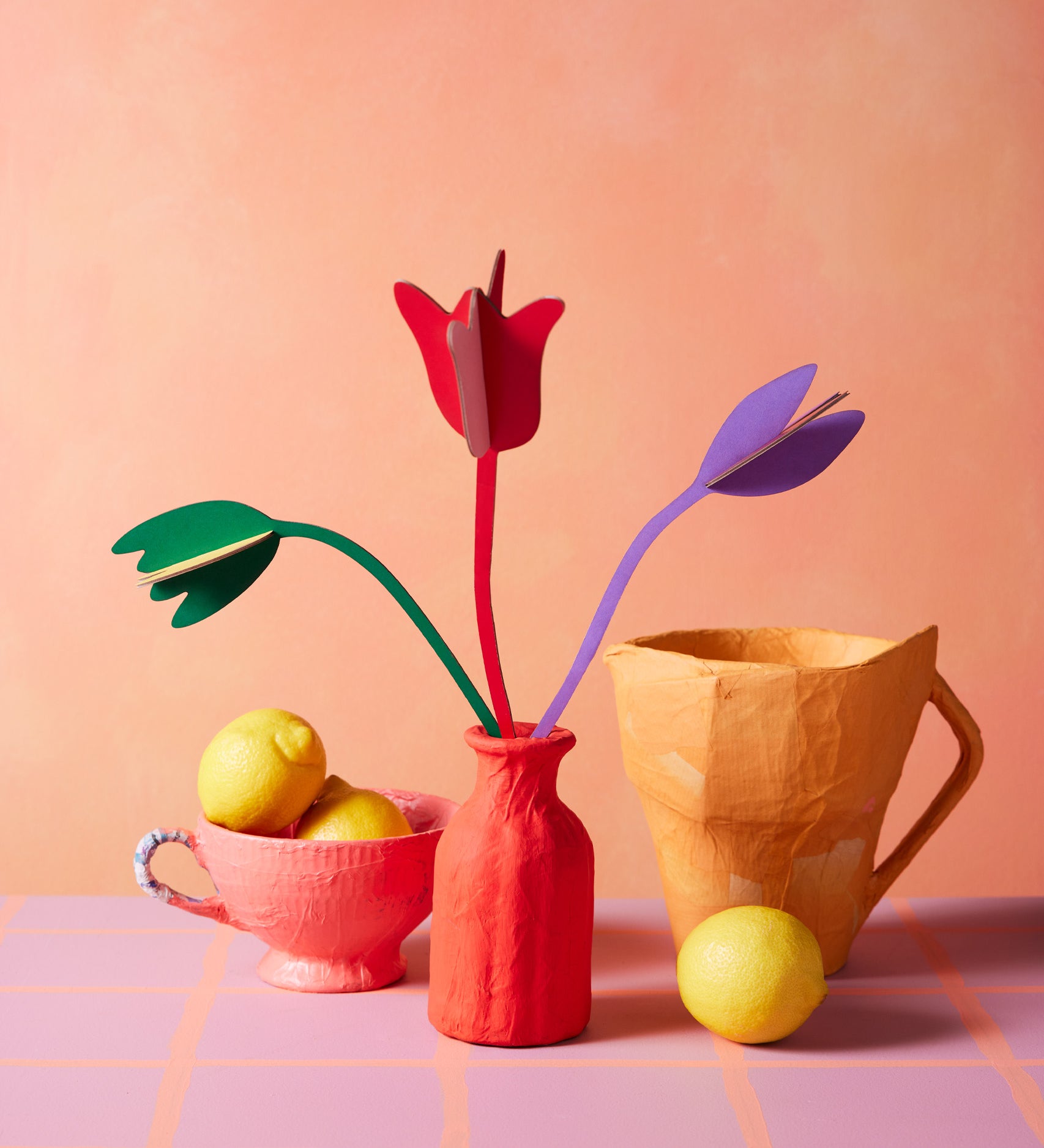 Studio Roof cardboard bouquet in tulip love colour way available at Babipur. A DIY kit made from cardboard displayed in a homemade red paper mache vase next to a watering jug and fruit bowl 