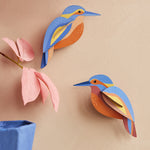 The Studio Roof Kingfishers are on a peach coloured wall, with a pink flower and blue vase in the bottom left corner of the photo