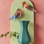 The Studio Roof Robins on a pink and green background, with a green vase and plant stem underneath the cardboard birds