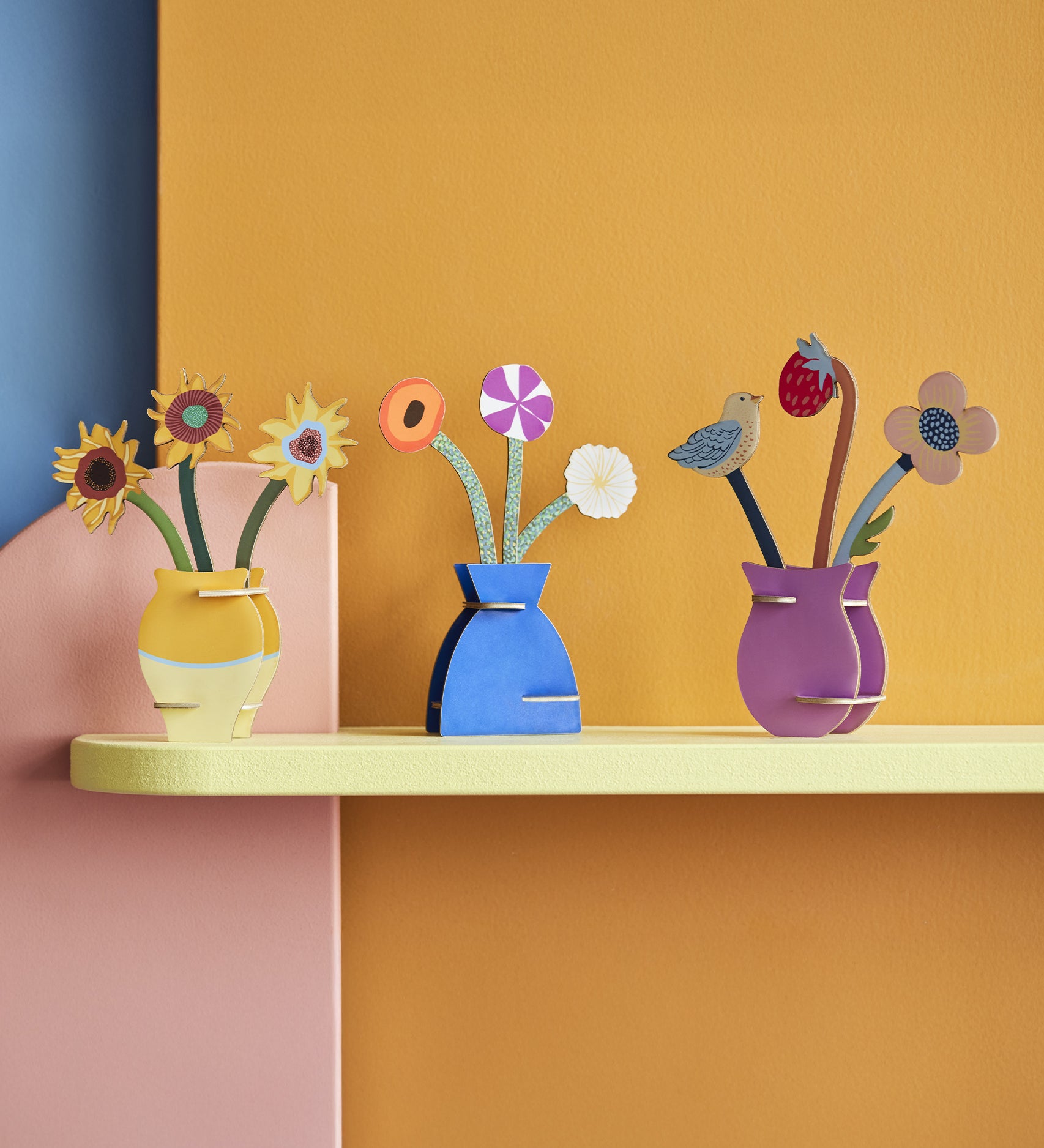 A selection of Studio Roof Pop Out cards on a yellow shelf, with a yellow, pink and blue background