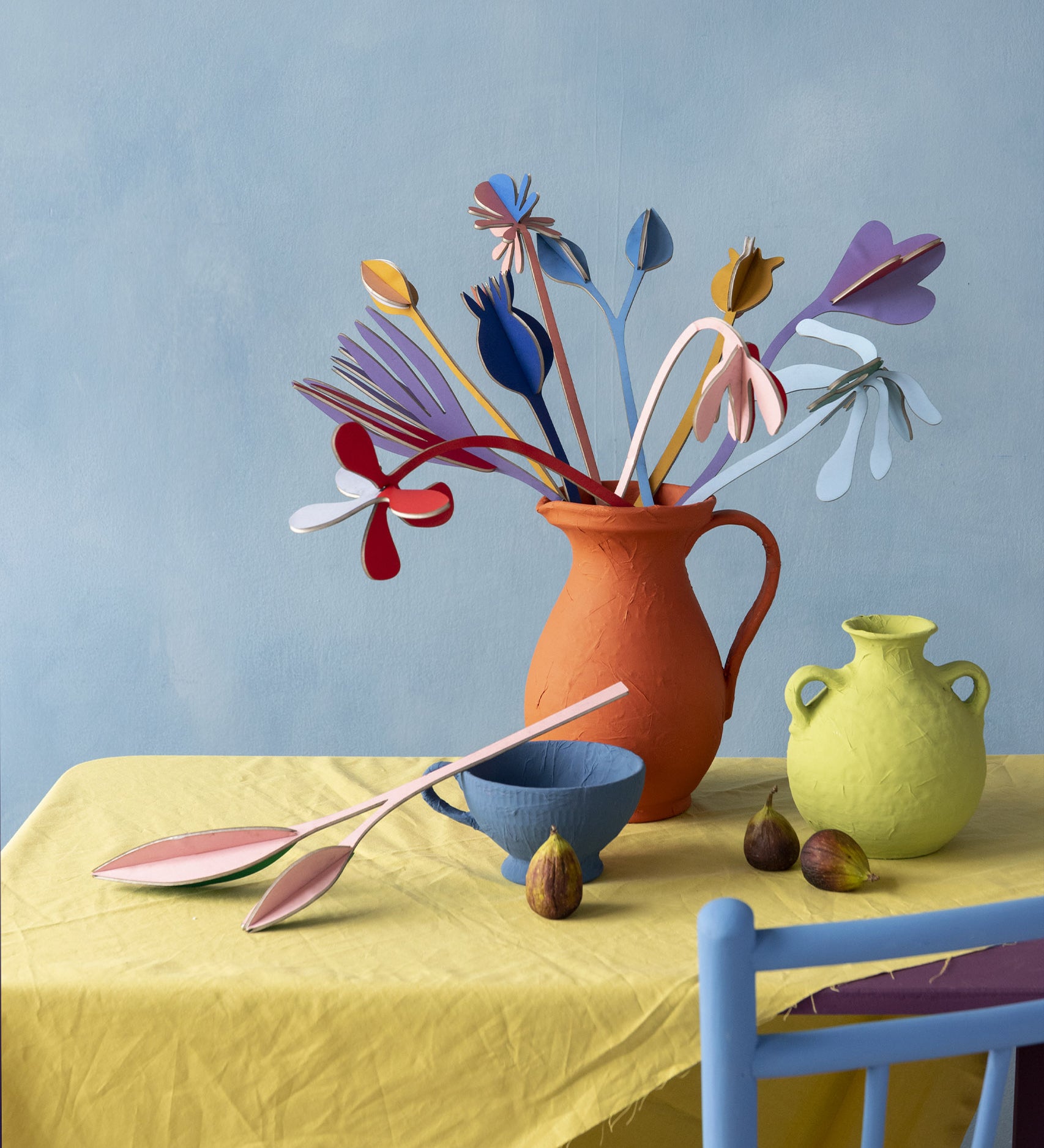 Studio Roof giant cardboard bouquet in available at Babipur. A DIY kit made from cardboard in a shape of different coloured flowers. This set is displayed on a table in a home made red vase.
