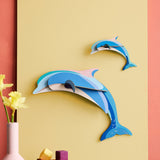 Studio Roof dolphin couple wall decoration available at Babipur hanging on a yellow board against a lightly coloured wall