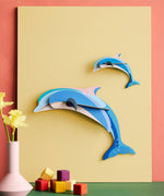 Studio Roof dolphin couple wall decoration available at Babipur hanging on a yellow board against a lightly coloured wall