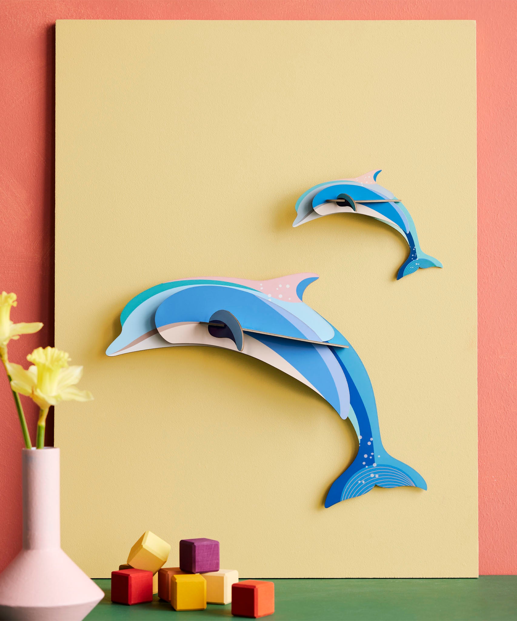Studio Roof dolphin couple wall decoration available at Babipur hanging on a yellow board against a lightly coloured wall
